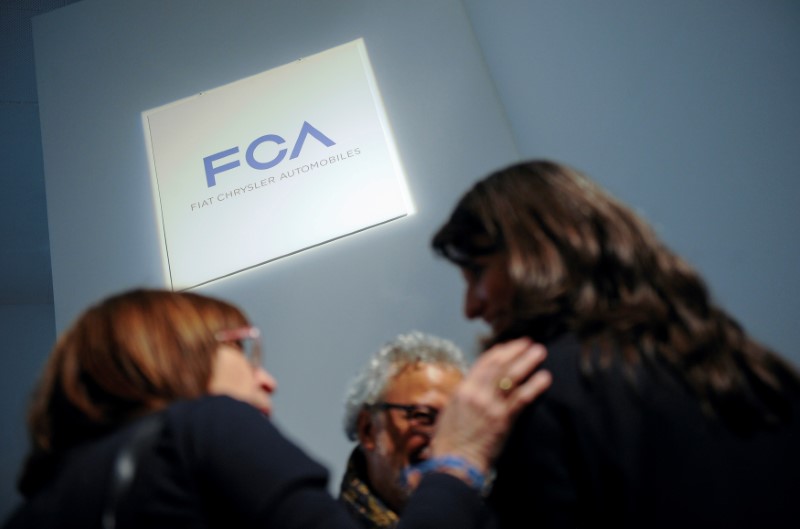 © Reuters. FILE PHOTO: People talk as they stand next to a logo of Fiat Chrysler Automobiles (FCA) in Turin