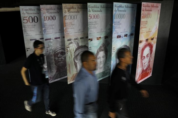 © Reuters. Pessoas  passam por cartazes do bolívar venezuelano no prédio do Banco Central em Caracas, Venezuela