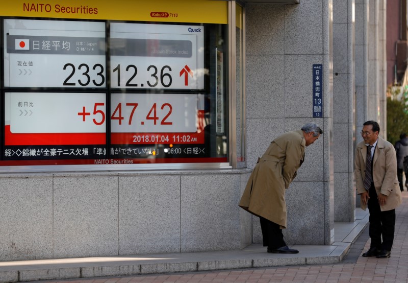 © Reuters. Men exchange greetings in front of an electronic board displaying the Nikkei average outside a brokerage in Tokyo