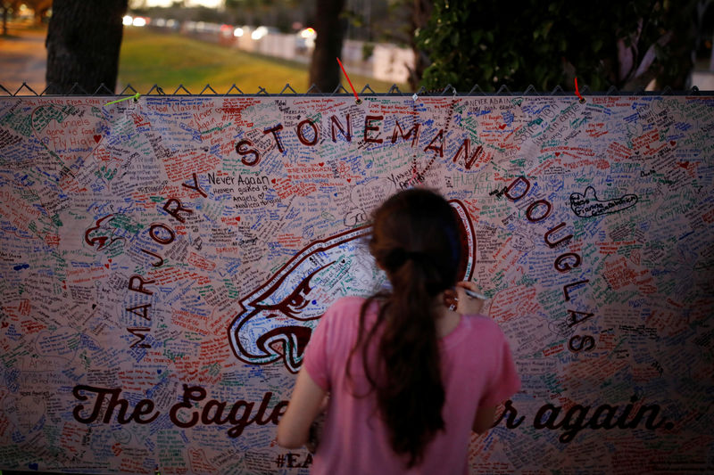 © Reuters. A girl writes a note on a banner placed on the fence of the Marjory Stoneman Douglas High School to commemorate the victims of the mass shooting, in Parkland