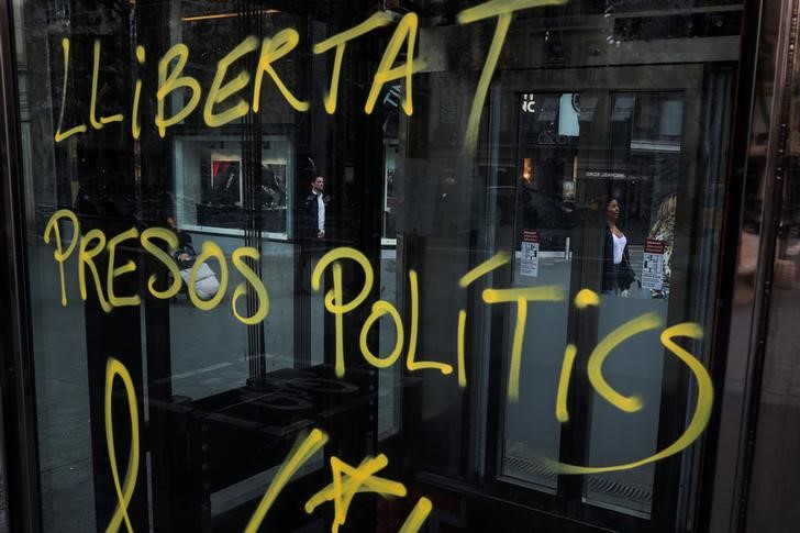 © Reuters. People walk by graffiti that reads 'Freedom for political prisoners' a day after former president Carles Puigdemont was detained in Germany, on a street in Barcelona