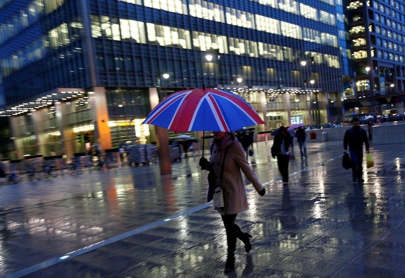 © Reuters. FILE PHOTO - Workers walk in the rain at the Canary Wharf business district in London