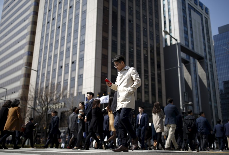 © Reuters. A man using his mobile phone walks on a zebra crossing at a business district in Seoul