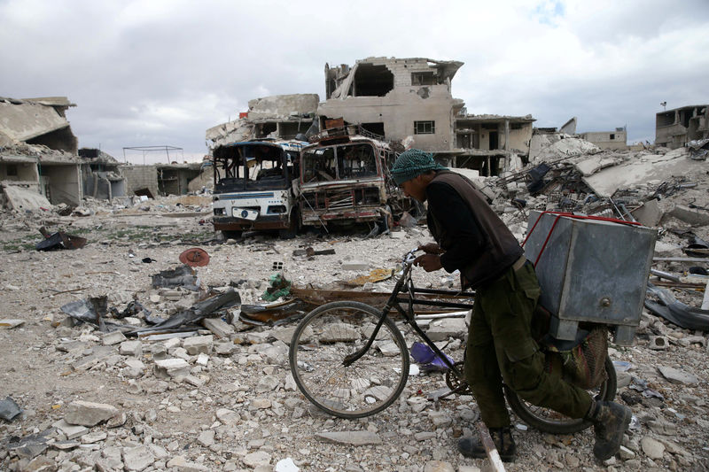 © Reuters. Un hombre camina junto a su bicicleta en un sitio dañado en la sitiada ciudad de Douma