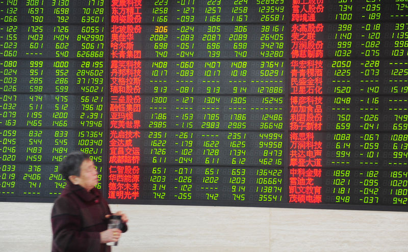 © Reuters. Woman walks past an electronic board showing stock information at a brokerage house in Fuyang, Anhui