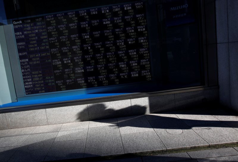 © Reuters. A pedestrian casts a shadow in front of an electronic stock quotation board outside a brokerage in Tokyo, Japan