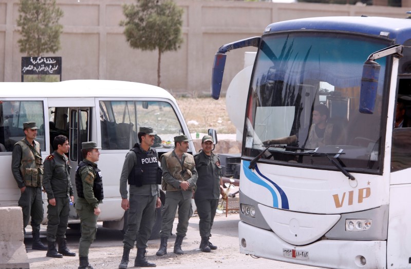 © Reuters. Soldados del Ejército sirio aparecen de pie junto a autobuses que transportan a rebeldes y sus familias, en Damasco