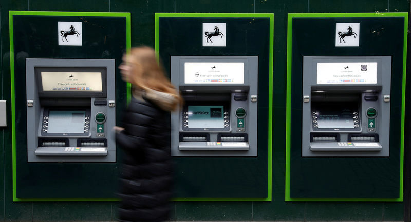 © Reuters. FILE PHOTO: A woman walks past a row of cash machines outside a branch of Lloyds Bank in Manchester
