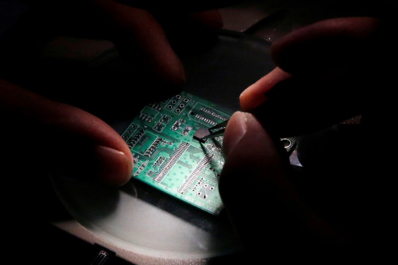 © Reuters. FILE PHOTO: A researcher plants a semiconductor on an interface board which is placed under a microscope during a research work to design and develop a semiconductor product at Tsinghua Unigroup research centre in Beijing