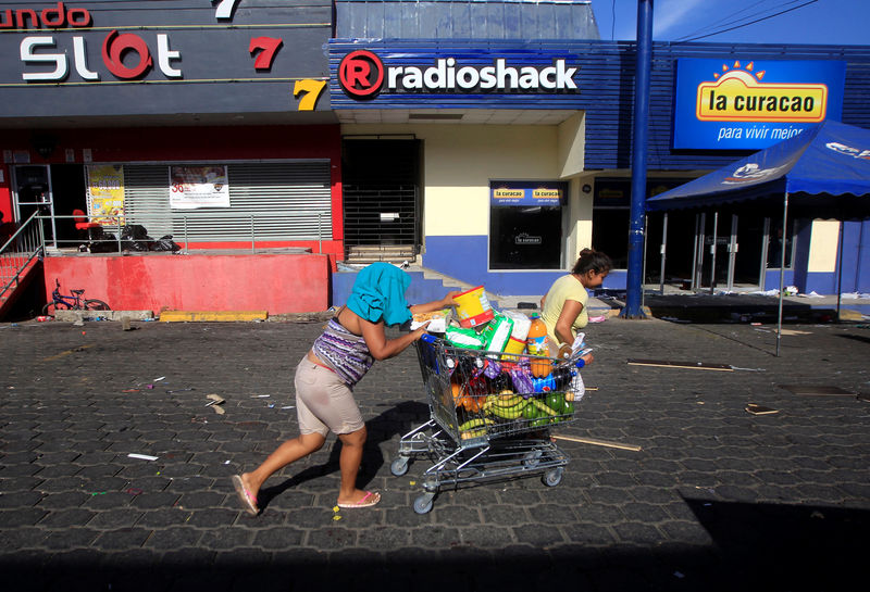 © Reuters. A woman with goods looted from a store walks pushing a shopping trolley along a street after protests in Managua