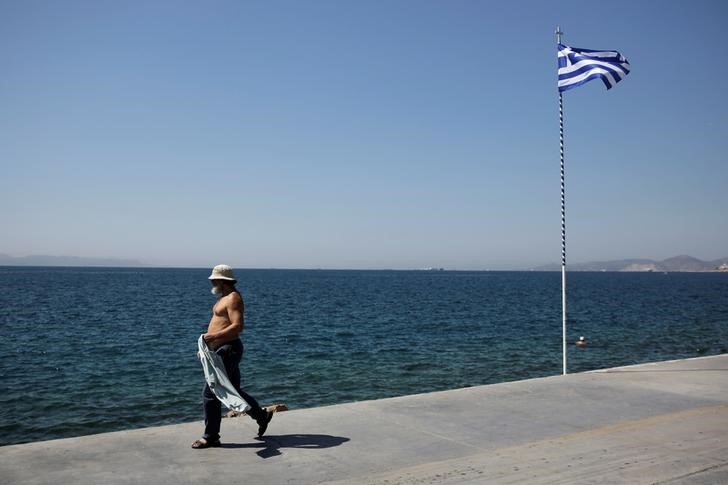 © Reuters. A man walks among seaside as a greek flag flutters at Faliro suburb near Athens