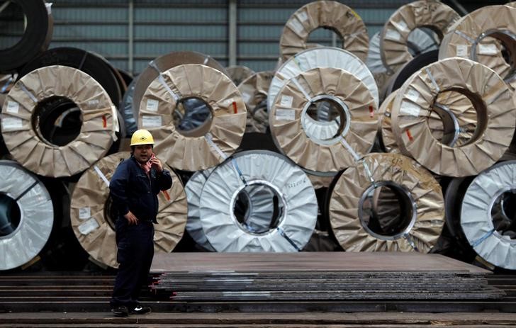 © Reuters. A worker uses a mobile phone in front of steel coils and steel sheets at a distribution warehouse in Urayasu