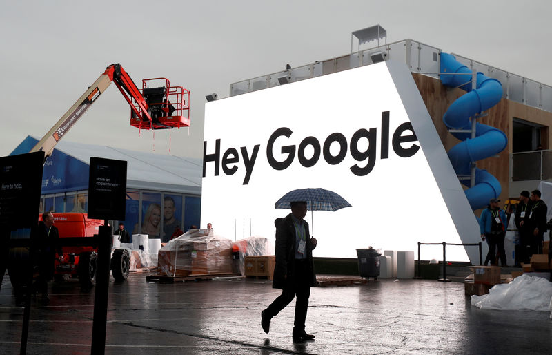 © Reuters. FILE PHOTO: A man walks through light rain in front of the Hey Google booth under construction at the Las Vegas Convention Center in preparation for the 2018 CES in Las Vegas