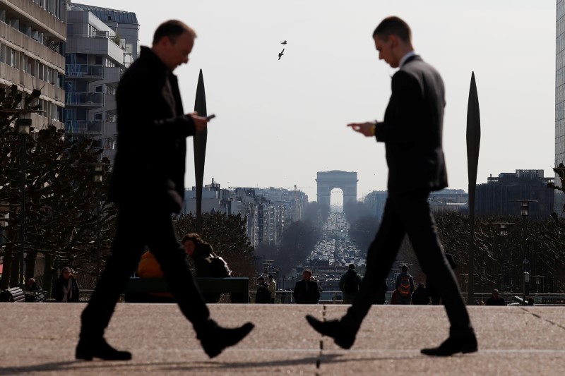 © Reuters. Men look at their mobile phones as they walk on the esplanade of La Defense in the financial and business district of La Defense, west of Paris