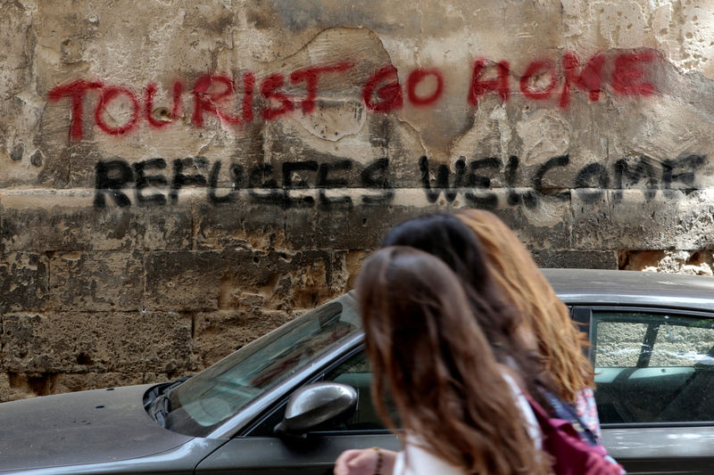© Reuters. FILE PHOTO: People walk past a graffiti in Palma de Mallorca