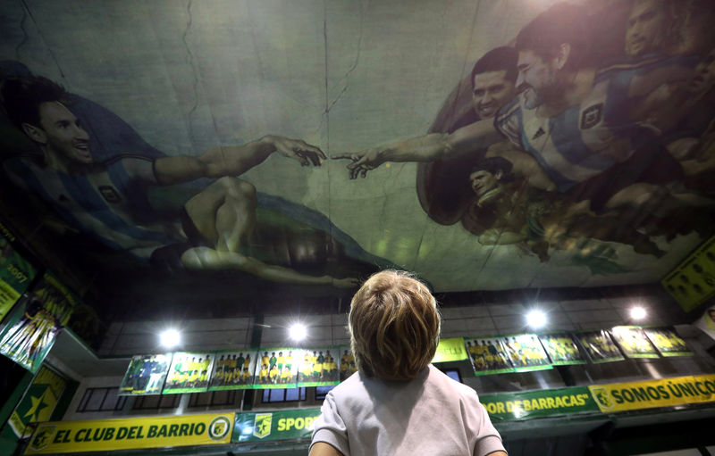 © Reuters. A boy looks at images of Messi and Maradona depicted on the ceiling in a recreation of Michelangelo's Sistine Chapel painting at Sportivo Pereyra club in Buenos Aires