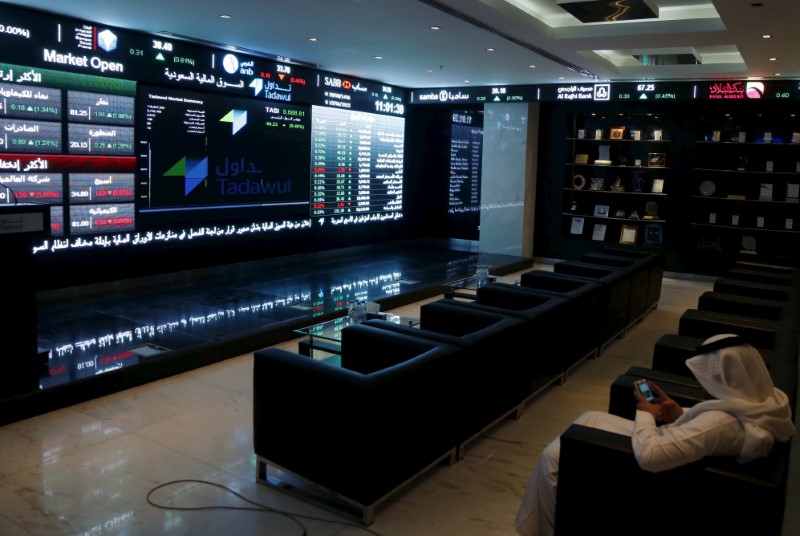 © Reuters. FILE PHOTO: A trader uses his mobile as he monitors screens displaying stock information at the Saudi Stock Exchange (Tadawul) in Riyadh