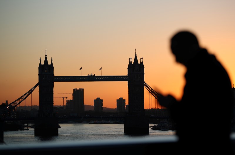 © Reuters. A man walks across London Bridge as the sun rises behind Tower Bridge in London