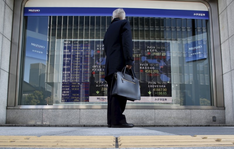 © Reuters. A pedestrian stands to look at an electronic board showing the stock market indices of various countries outside a brokerage in Tokyo