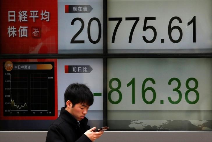 © Reuters. Man looks at a mobile phone in front of an electronic board showing Japan's Nikkei average outside a brokerage in Tokyo