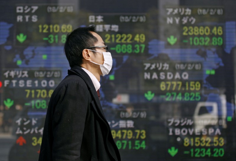 © Reuters. A man walks past an electronic board showing the stock market indices of various countries outside a brokerage in Tokyo