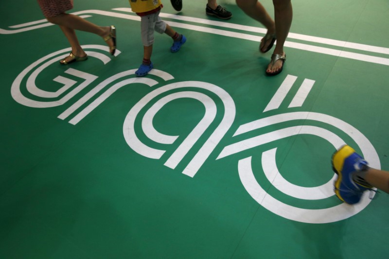 © Reuters. FILE PHOTO: Commuters walk past a Grab transport booking service app advertisement at a train station in Singapore