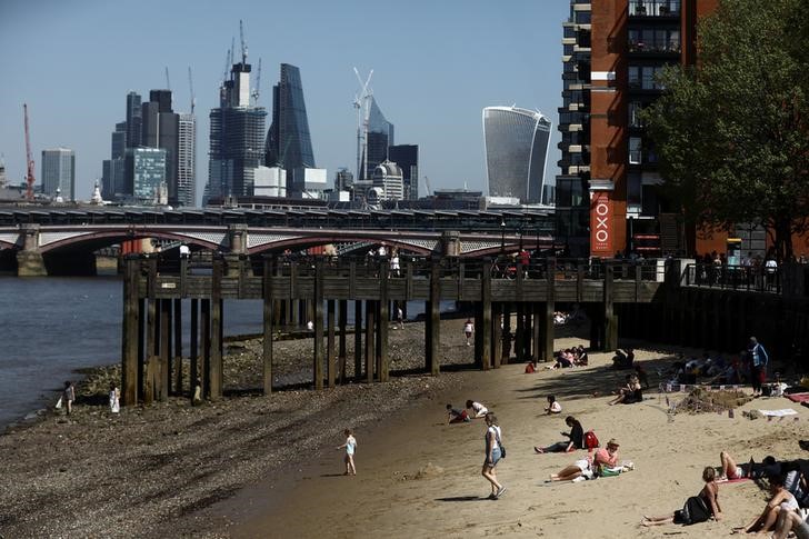 © Reuters. People sunbathe on the banks of the River Thames in view of London financial district in London