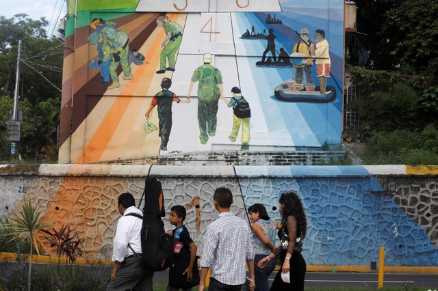 © Reuters. Una familia pasa junto a un mural que representa el viaje de los migrantes centroamericanos a Estados Unidos, en San Salvador, El Salvador