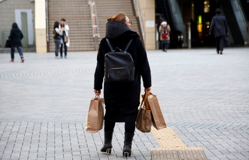 © Reuters. FILE PHOTO: A woman holds shopping bags as she stands in front of a railway station in Tokyo