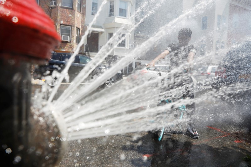 © Reuters. A boy on a bicycle cools off from the extreme heat from an opened fire hydrant in Brooklyn, New York