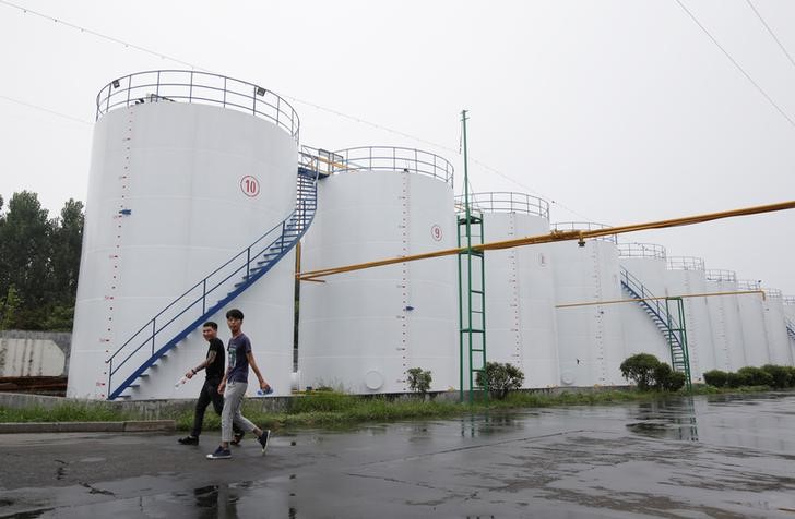 © Reuters. Люди проходят рядом с нефтяными резервуарами на предприятии компании Liangyou Industry and Trade Co., Ltd в городе Цюйфу в китайской провинции Шаньдун