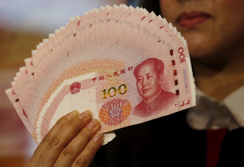 © Reuters. FILE PHOTO: A staffer poses with 2015 edition of the 100 renminbi notes at the Bank of China Tower in Hong Kong