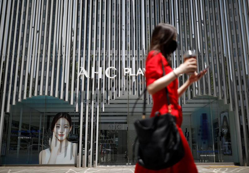 © Reuters. A woman holding her mobile phone walks past an AHC cosmetic store in Seoul