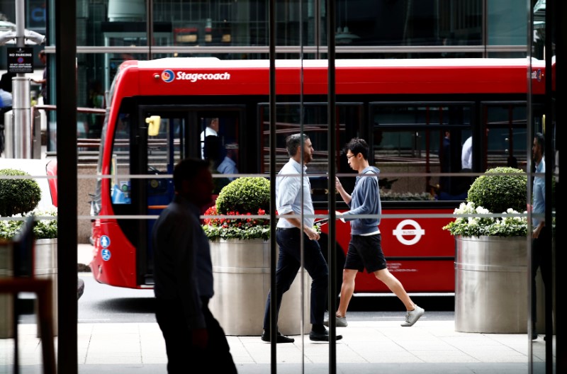 © Reuters. People walk past a bus in the financial district of Canary Wharf