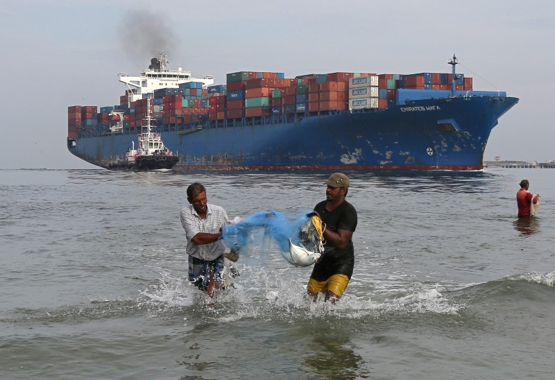 © Reuters. FILE PHOTO: Fishermen carry bluefin trevally fish locally known as Vatta as a cargo ship carrying containers moves in the Arabian Sea in Kochi,