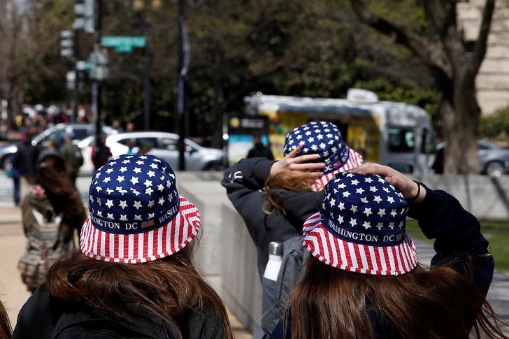 © Reuters. Girls wearing hats with an U.S. flag motif hold them down during windy weather in Washington