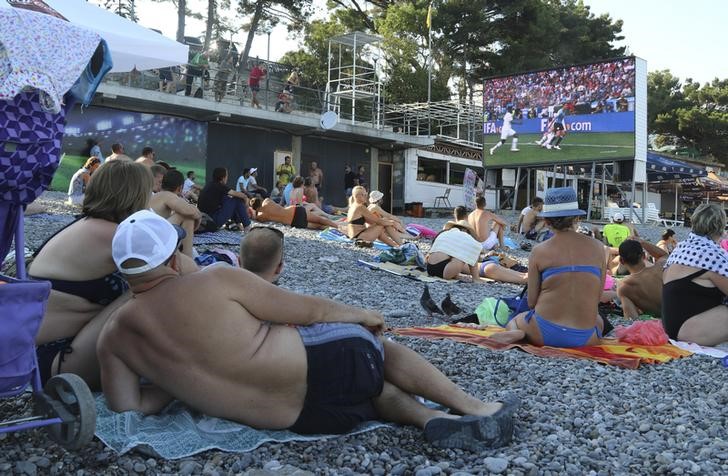 © Reuters. Люди смотрят матч 1/4 финала футбольного ЧМ-2018 между Францией и Уругваем на пляже в Ялте