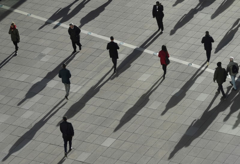 © Reuters. FILE PHOTO: People cast long shadows in the winter sunlight as they walk across a plaza in the Canary Wharf financial district of London