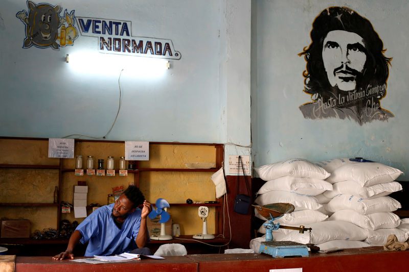 © Reuters. A man works in a subsidised state store, or "bodega", next to an image of late revolutionary hero Ernesto "Che" Guevara in Havana