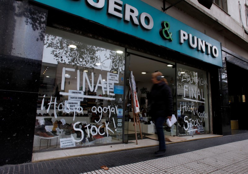 © Reuters. A woman walks past a store that displays signs and grafittis that read "final sale while supplies" in Buenos Aires