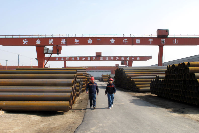 © Reuters. FILE PHOTO: Workers walk past steel pipes at a steel mill in Cangzhou