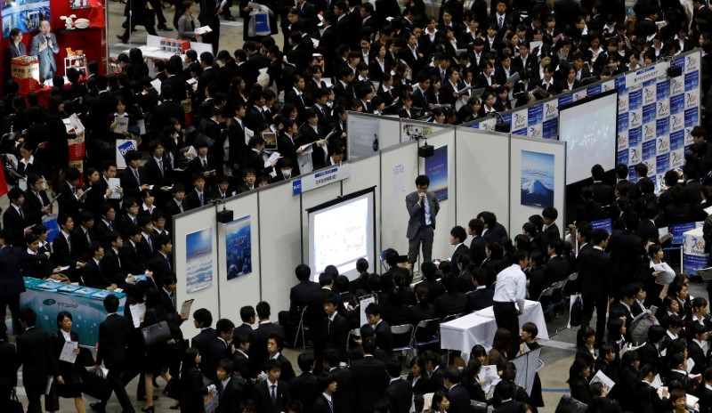 © Reuters. FILE PHOTO: Job seekers listen to presentations at company booths during a job fair held for fresh graduates in Tokyo