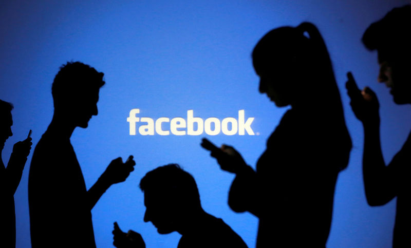 © Reuters. FILE PHOTO: People pose with mobile devices in front of projection of Facebook logo in this picture illustration taken in Zenica