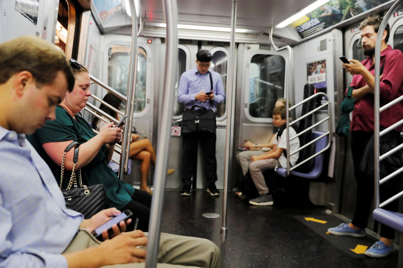 © Reuters. Commuters use their mobile phones as they ride a subway train in New York