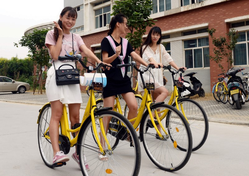 © Reuters. Alunas posam para fotos com bicicletas de compartilhamento Ofo em campus universitário de Zhengzhou