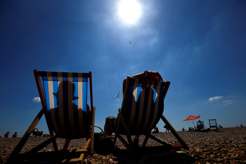 © Reuters. FILE PHOTO: Visitors relax on deckchairs in the sunshine on the beach by Brighton Pier in Brighton