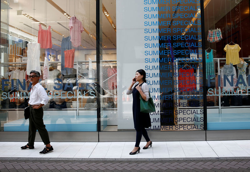 © Reuters. Pedestrians stand in front of sale signs on a shopfront at a shopping district in Tokyo