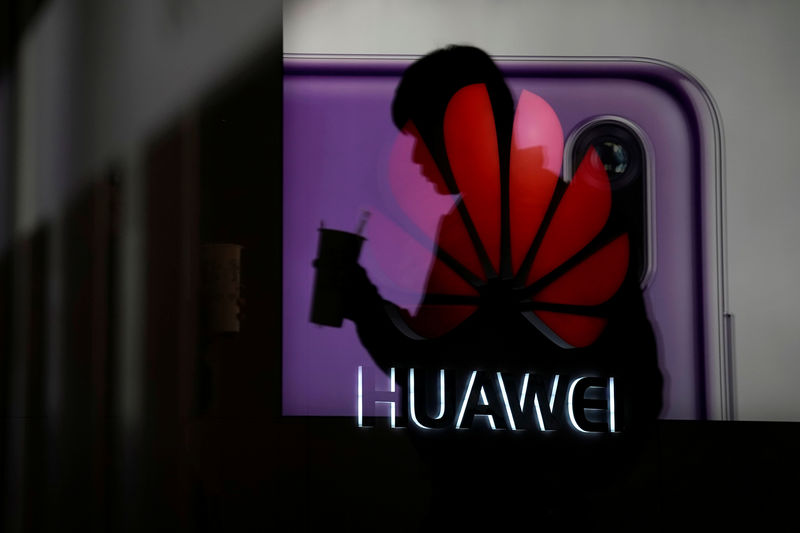 © Reuters. A man walking past a Huawei P20 smartphone advertisement is reflected in a glass door in front of a Huawei logo, at a shopping mall in Shangha