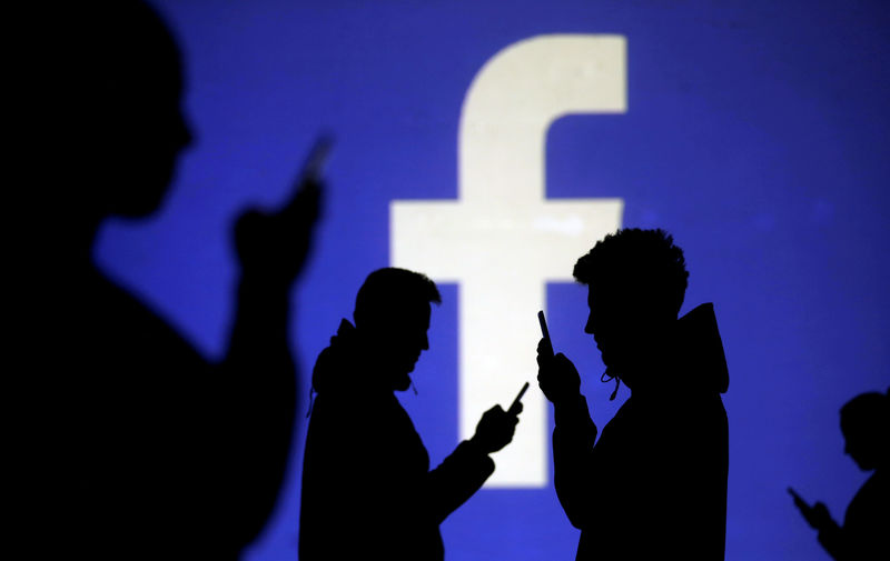 © Reuters. FILE PHOTO: Silhouettes of mobile users are seen next to a screen projection of Facebook logo in this picture illustration