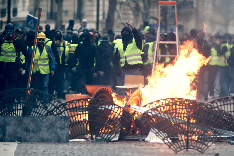 © Reuters. Protesters wearing yellow vests stand behind a barricade as they face off with police during clashes as part of a national day of protest by the "yellow vests" movement in Paris